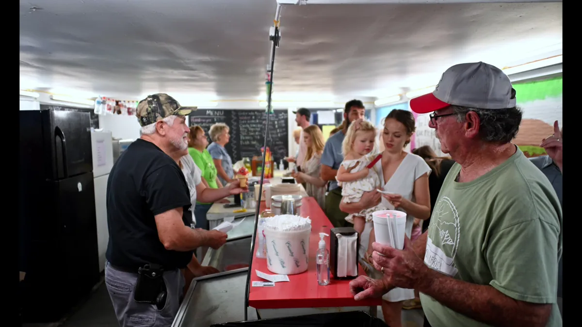 The snack bar counter, three generations queueing along it.