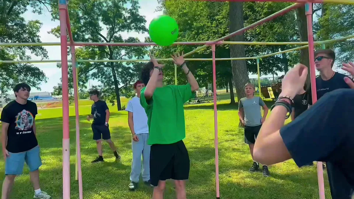A camper reaching up to play the ball through a painted metal frame during a lawn game.