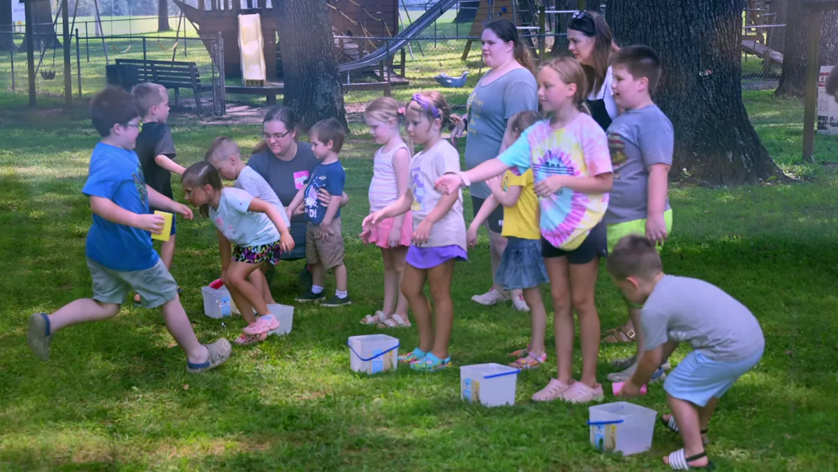 Campers running a water-bucket relay on the lawn